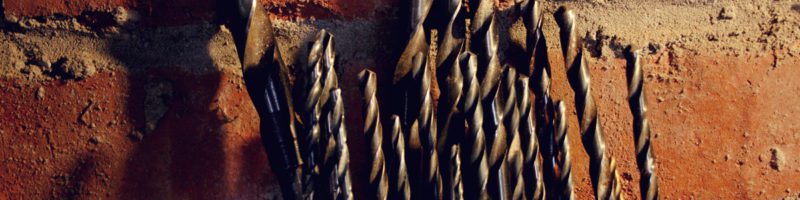 drill bits in a block against a brick wall