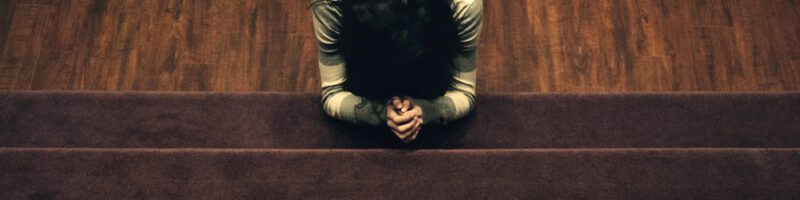 woman kneeling in prayer on a wood floor in front of the stairs