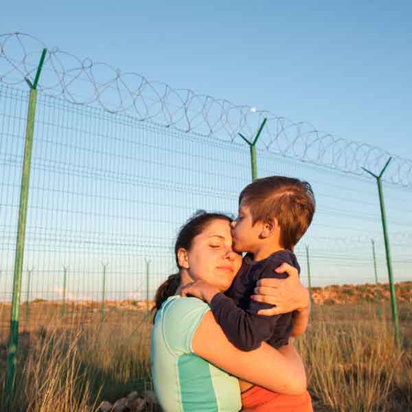 woman hugging son in front of a prison fence