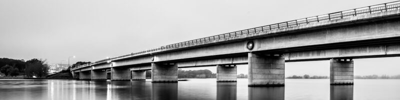 a long bridge over a river in a black and white photograph