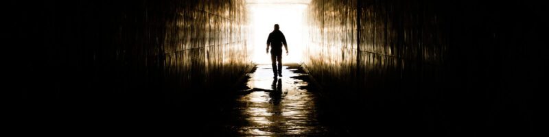 photo of man walking into a dark tunnel with bright light behind him